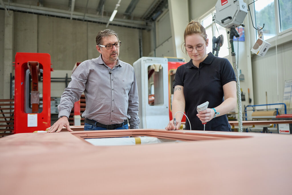 Ein Mann und eine Frau prüfen und messen ein großes industrielles Bauteil in einer Fabrik oder Werkstatt. LAC Berger Industrielackierung