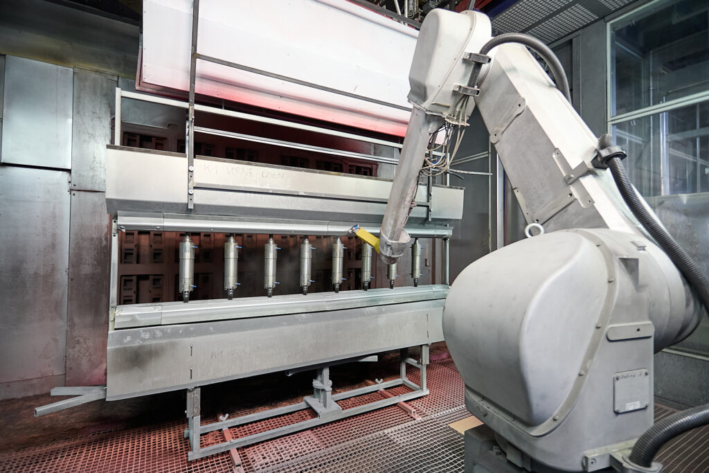 Ein Roboterarm arbeitet in einer Industrieanlage in der Nähe einer Metallbearbeitungs- oder Montagemaschine in einer Fertigungsumgebung. LAC Berger Industrielackierung